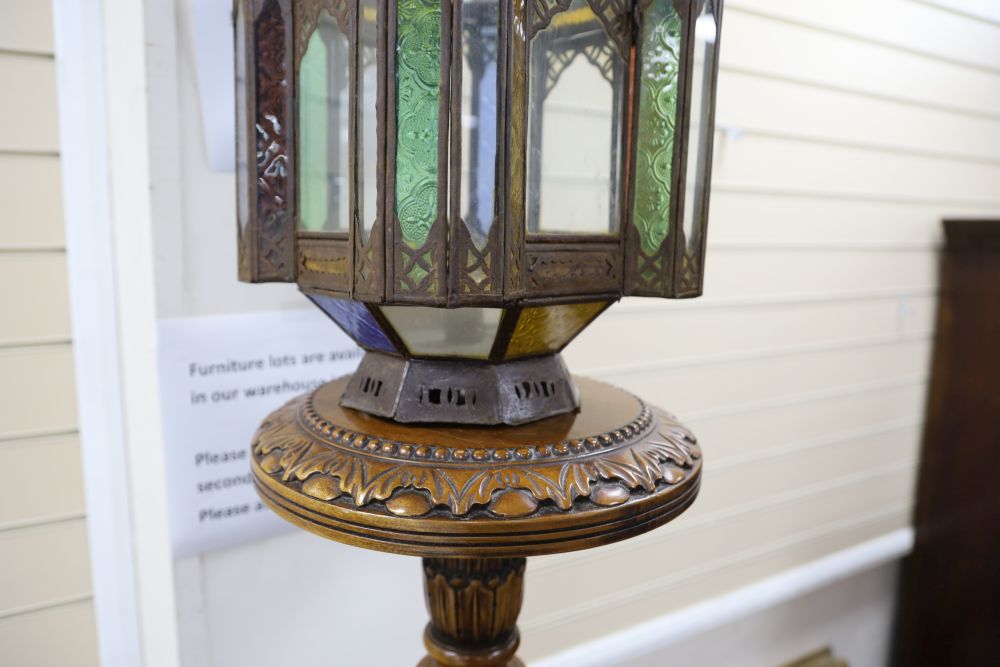 A pierced metal lantern with coloured glass panes, on carved walnut triform pedestal, 206cm overall